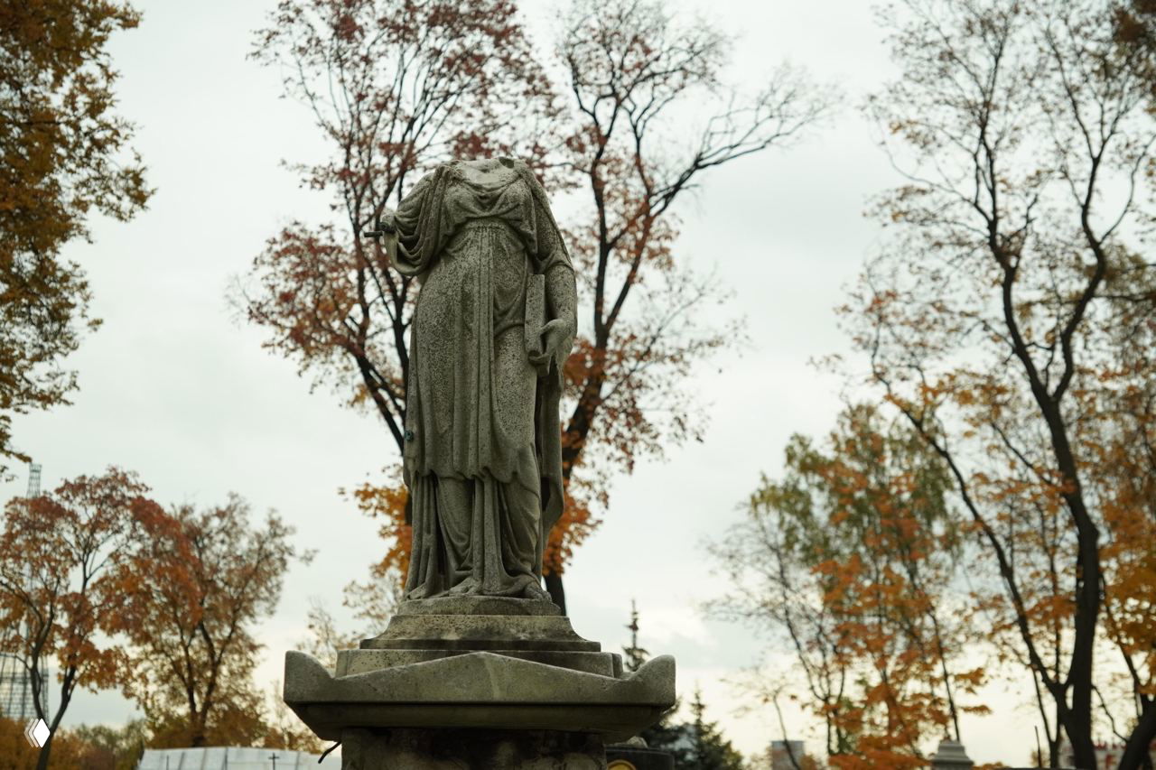 Статуя без головы в образе памятника на фоне голых деревьев и пасмурного неба на территории Донского некрополя