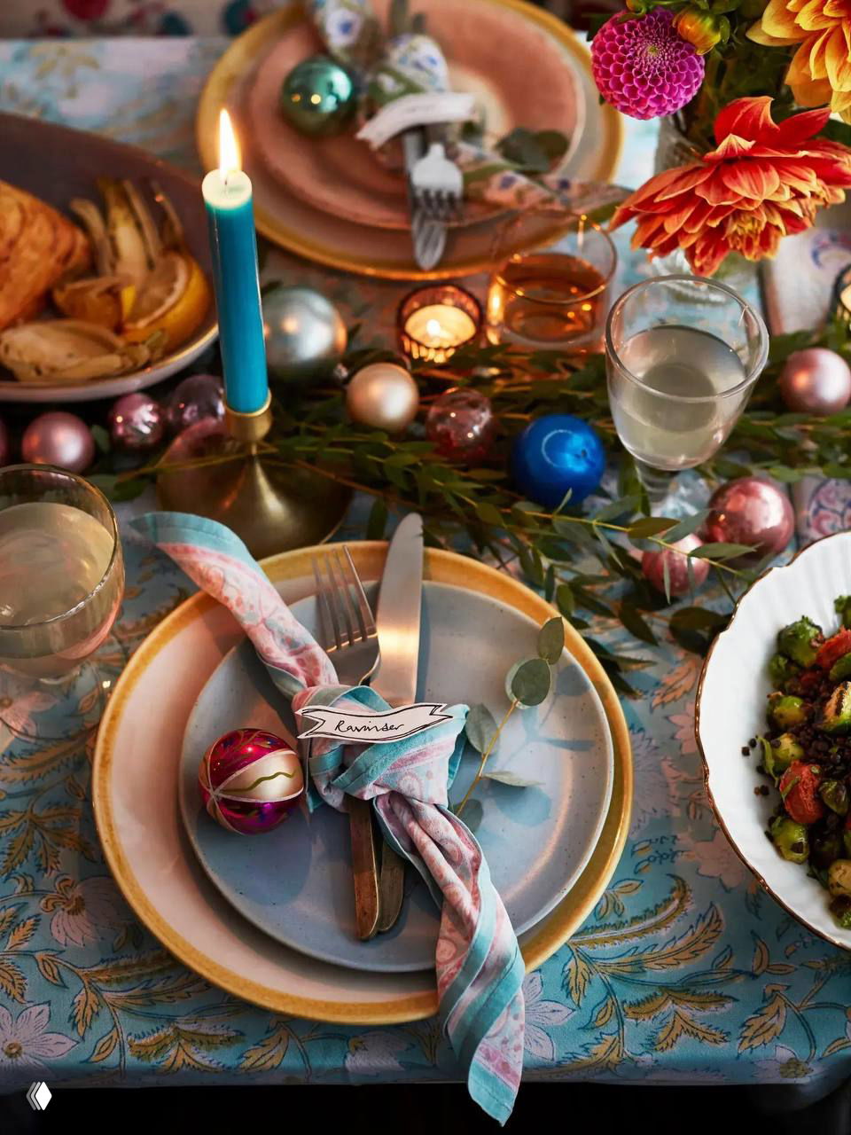 Крупный план сервировки: тарелки, тканевые салфетки, свеча и праздничные шарики в композиции — внимание к деталям и текстурам на столе.