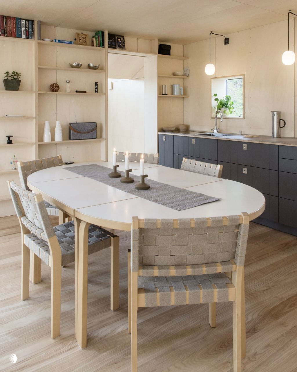 Обеденная зона и минималистичная кухня: плетёные стулья, продуманная система хранения и ровный светлый деревянный пол в небольшом доме.