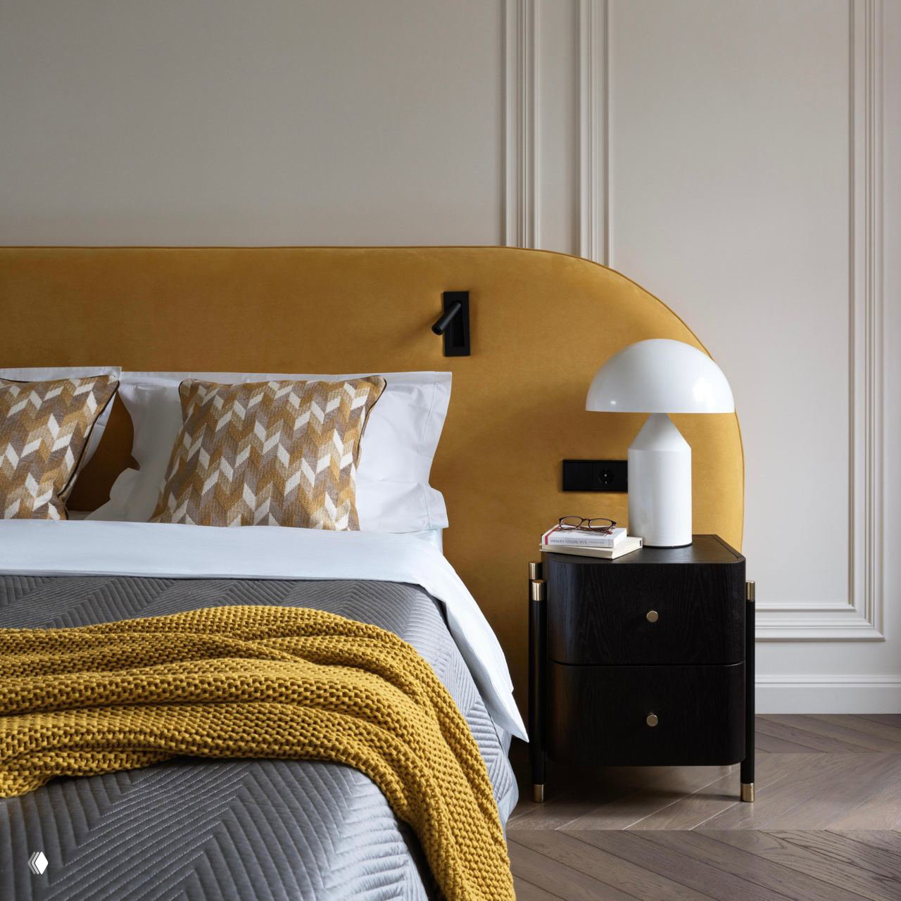 Спальня с округлым изголовьем охрового оттенка, вязанный горчичный плед и тумба из тёмного дерева у кровати в нейтральной комнате.