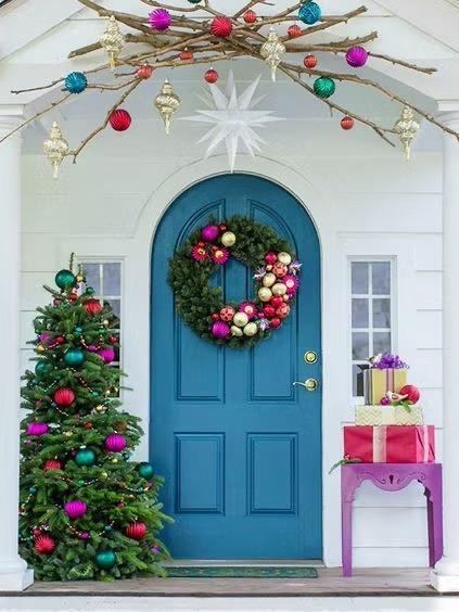 Бирюзовая входная дверь с круглым венком и рядом украшенная небольшая праздничная ёлка и подарки — яркая разноцветная композиция для праздничного внешнего вида дома.