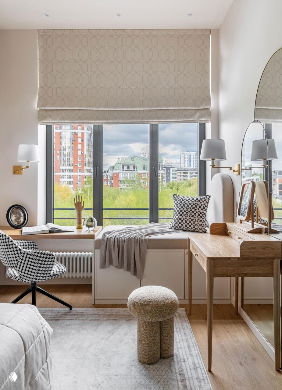 Окно в спальне с видом на город и рабочая зона: скамейка под окном, стильные настенные бра и цилиндрический пуф на текстурном ковре.