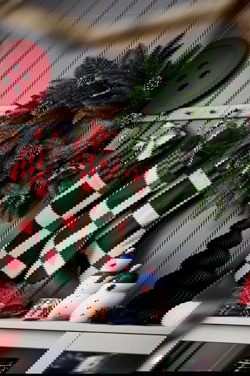 Клетчатые рождественские носки и зелёная хвоя на серой стене: сочетание красного и тёмно‑зелёного в текстурах и аксессуарах интерьера