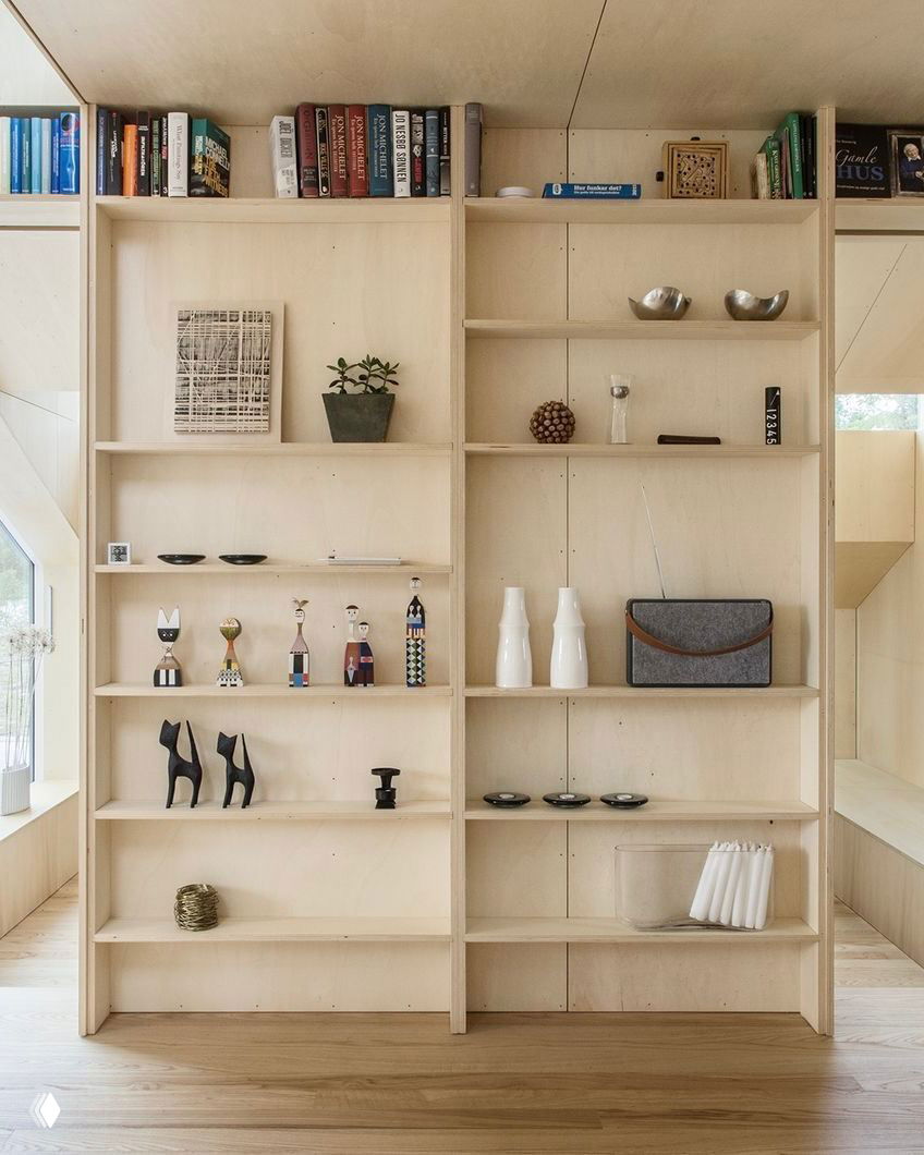 Открытые полки из светлой фанеры с книгами и аксессуарами на фоне деревянной отделки — минималистичный способ хранения и декора в домике Vindheim.