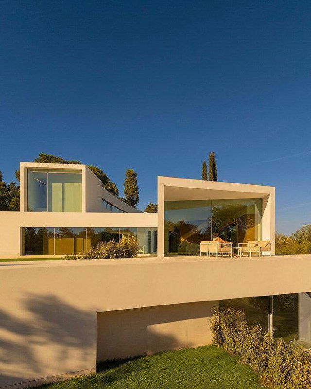 Фрагмент архитектурной композиции Villa Lago: белые плоскости и большие горизонтальные окна на фоне зелёных деревьев создают мягкий контраст и прозрачность.