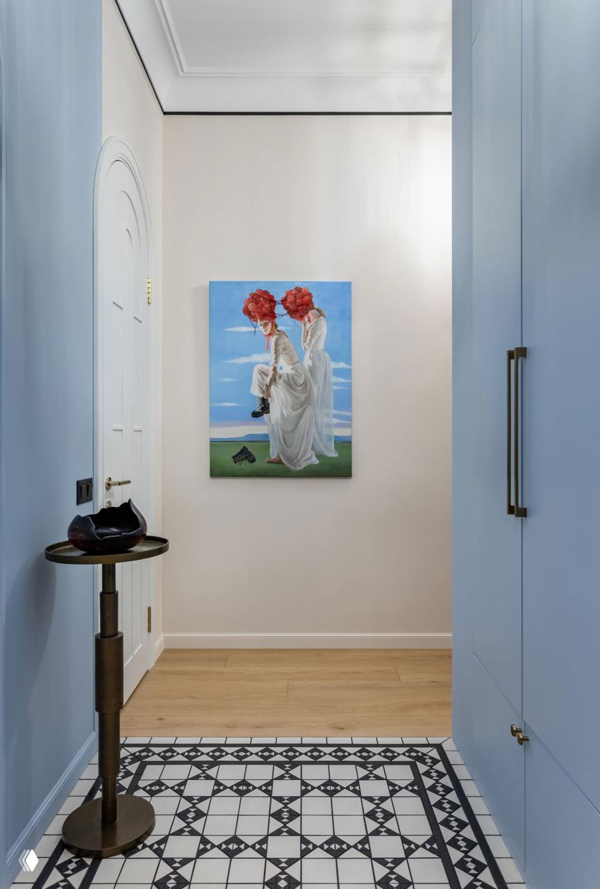 Узкий холл с голубыми стенами, декоративным ковром с чёрно-белым орнаментом и картиной с изображением девушек в красных платах — акцентный входной ансамбль.
