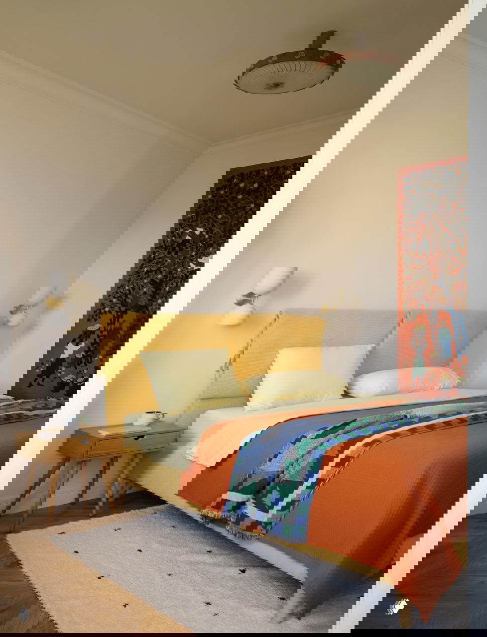 Рабочая зона и кровать в одном кадре: текстуры натурального дерева, мягкое кресло и пышные комнатные растения на голубой этажерке создают живой интерьер.