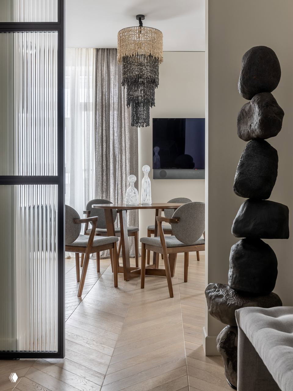 Обеденная зона и стулья в скандинавском стиле, крупная висящая люстра и декоративная инсталляция из камней у прохода, вид из гостиной на столовую.