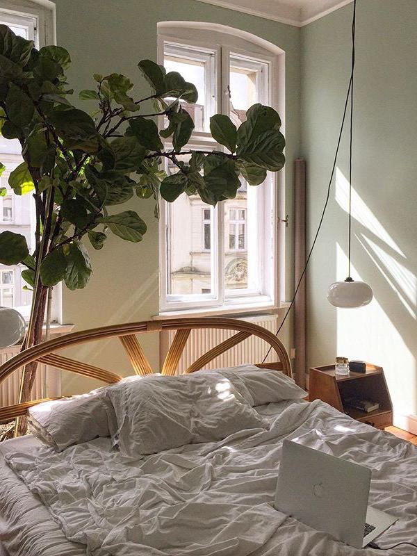 Уютная спальня с арочным плетёным изголовьем, широким окном и мягкими небрежно задрапированными простынями, много естественного света.