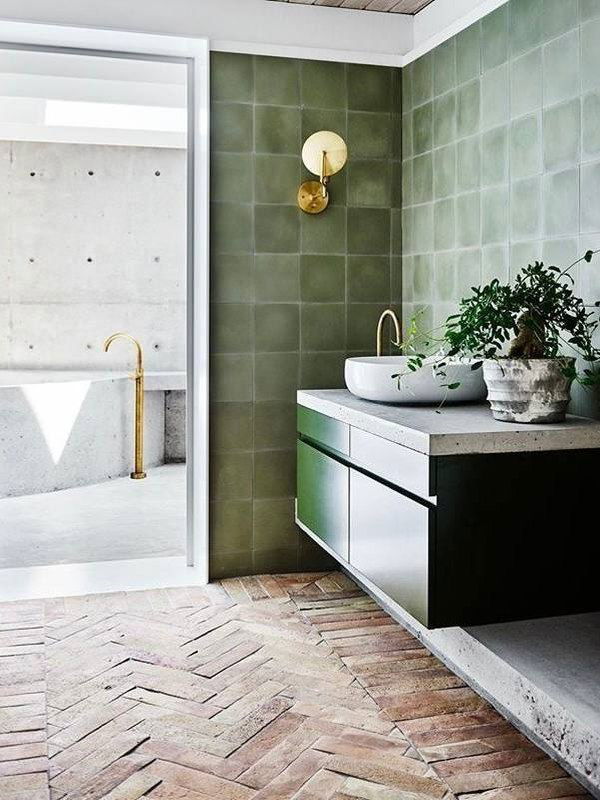 Ванная с матовой зелёной керамической плиткой оливкового тона, светлый бетонный умывальник, золотые смесители и живое растение на столешнице.
