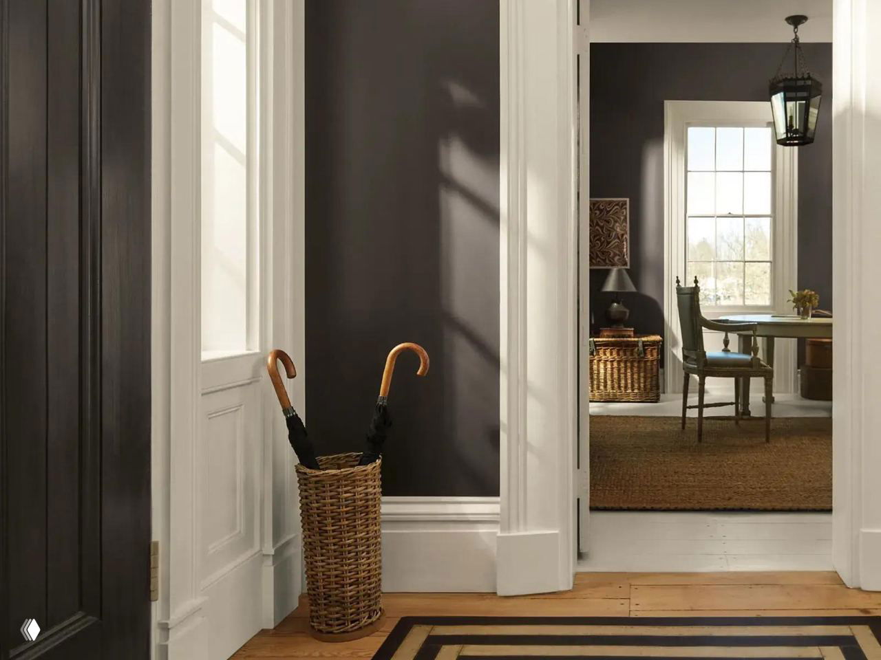 Интерьерный коридор с белыми наличниками и стеной, окрашенной в тёмный Silhouette; на полу деревянный настил и плетёная корзина с зонтами.