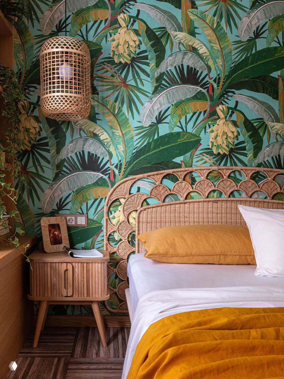 Ротанговое изголовье на фоне ярких тропических обоев, плетёная подвесная лампа и деревянная тумба создают экзотическую атмосферу в спальне.