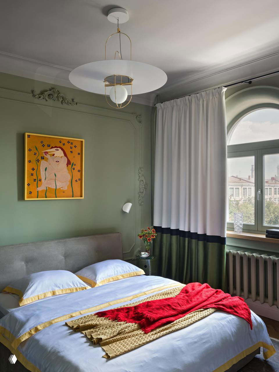 Комната-спальня с оливковыми стенами, светлый текстиль, яркие декоративные акценты и большое окно, пропускающее мягкий дневной свет в интерьер.