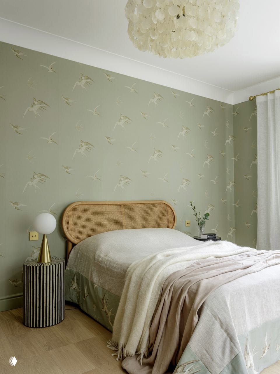 Спальня в пастельных тонах с плетёным низким изголовьем, обои с нежным орнаментом птиц и уютные текстильные слои на кровати.