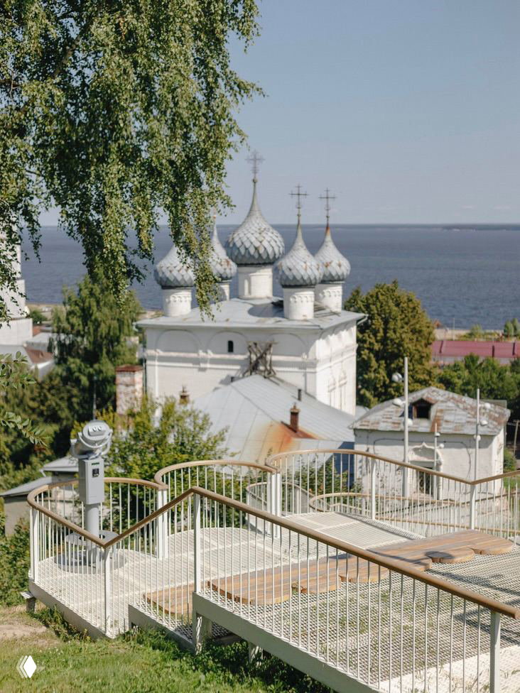 Белая ажурная лестница на склоне в Юрьевце с деревянными поручнями на фоне церкви и реки, вид с верхней точки.