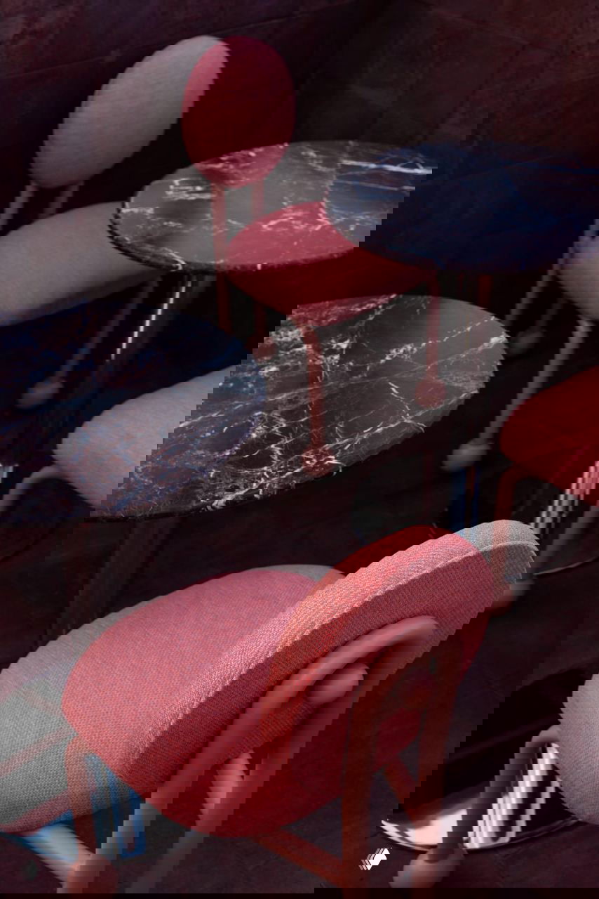 Низкие деревянные табуреты и розовые диванные секции на фоне тёмно‑красной плитки — контраст текстур дерева, ткани и пористого тесонтле на крыше отеля.