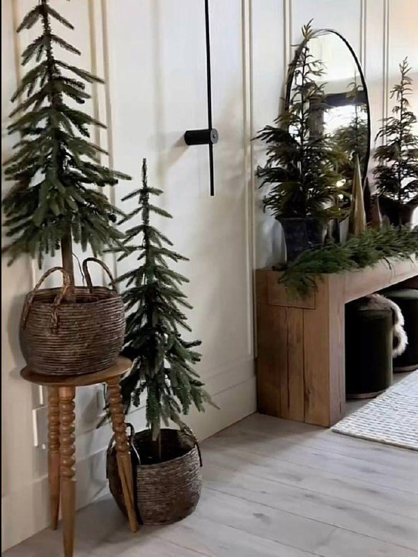 Тонкие ёлки в плетёных кашпо и декоративные зелёные композиции на деревянной консоли — натуральный минималистский праздничный декор.