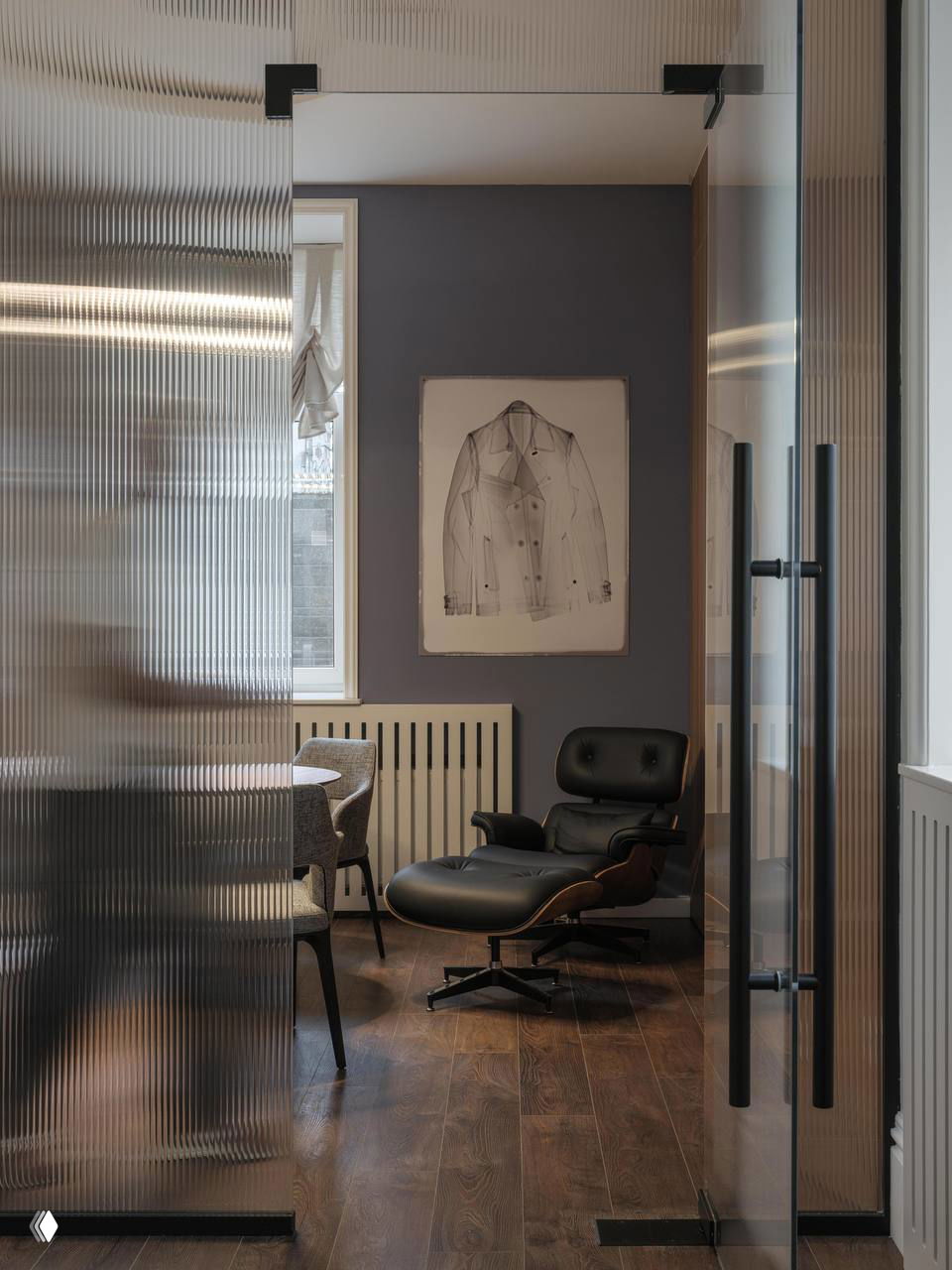 Проход и кабинет через рифлёное стекло: кресло Eames с оттоманкой, тёплый деревянный пол и спокойная минималистичная отделка для создания домашней атмосферы.