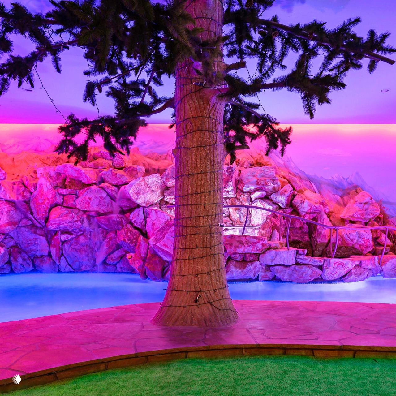 Внутренний двор с искусственным деревом, декоративными скалами и бассейном; неоновая подсветка создаёт насыщенные фиолетово‑розовые оттенки интерьера.