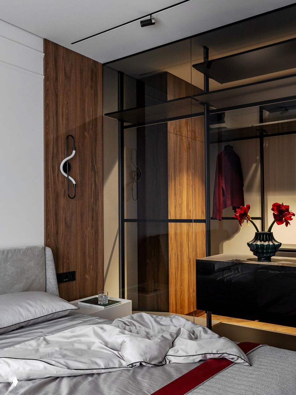 Спальня и гардеробная: деревянные панели, стеклянная перегородка и тёплое освещение; в кадре видно кровать с текстилем и сосудом с цветами как декоративный элемент.
