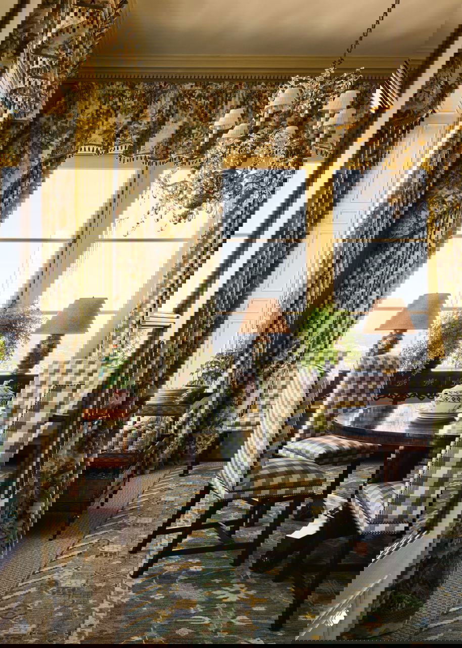 Столовая в стиле английской усадьбы: зелёные клетчатые стулья, пышные шторы с растительным орнаментом и хрустальная люстра — вид на город за окнами.