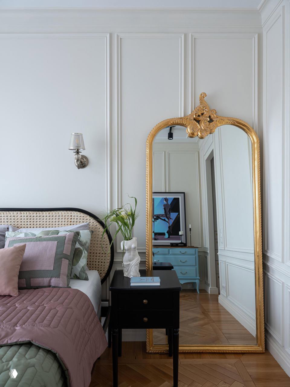 Классическая комната с тростниковым изголовьем и большим позолоченным зеркалом у стены, изысканная комбинация плетёного и антикварного декора.