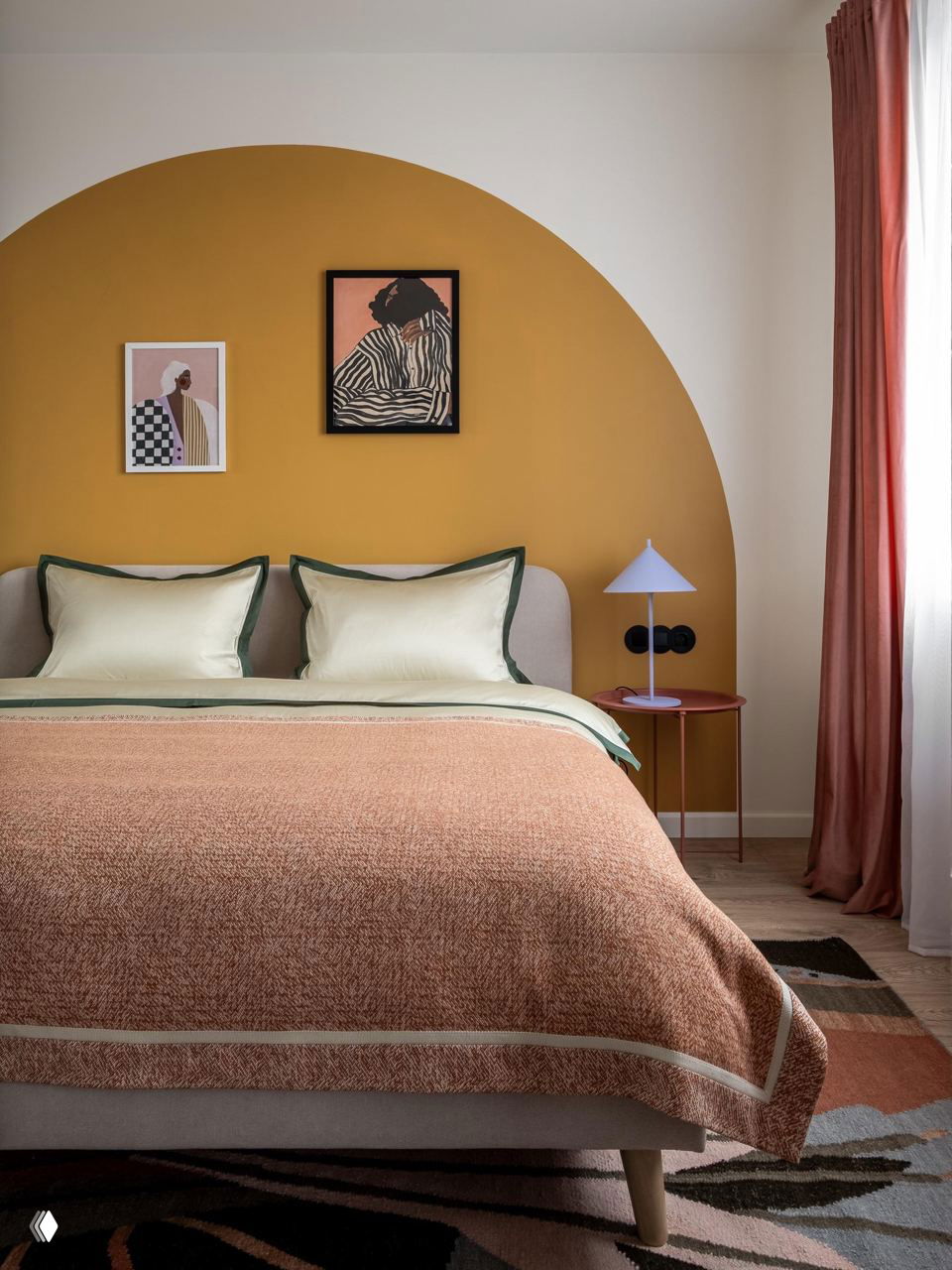 Спальня с полукруглой охристой акцентной стеной, нежными постельными тонами и текстильными шторами; сочетание тёплых и холодных акцентов для баланса пространства.
