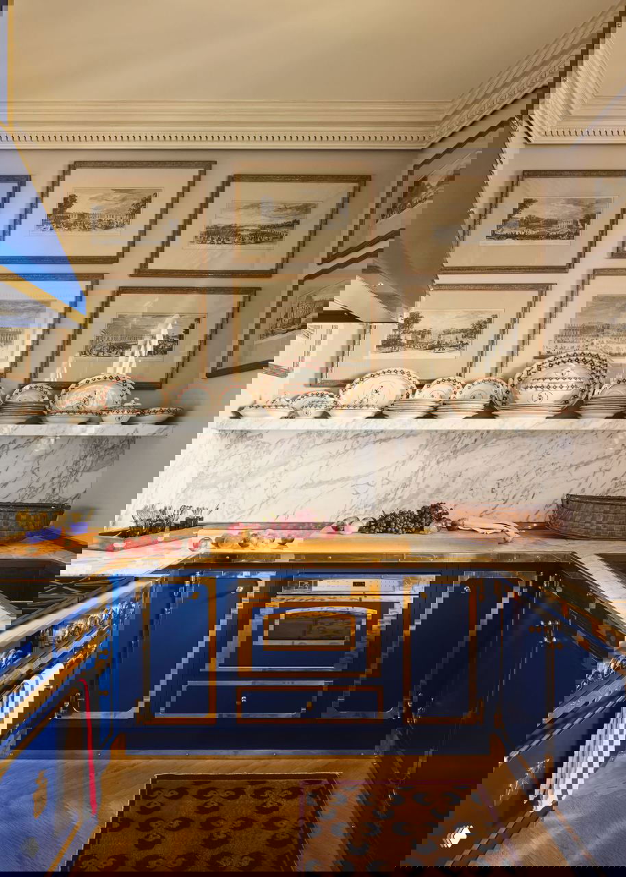 Кухня с синими шкафами и золотистой отделкой, мраморная столешница и коллекция фарфора на полке — классический интерьерный ансамбль пентхауса.