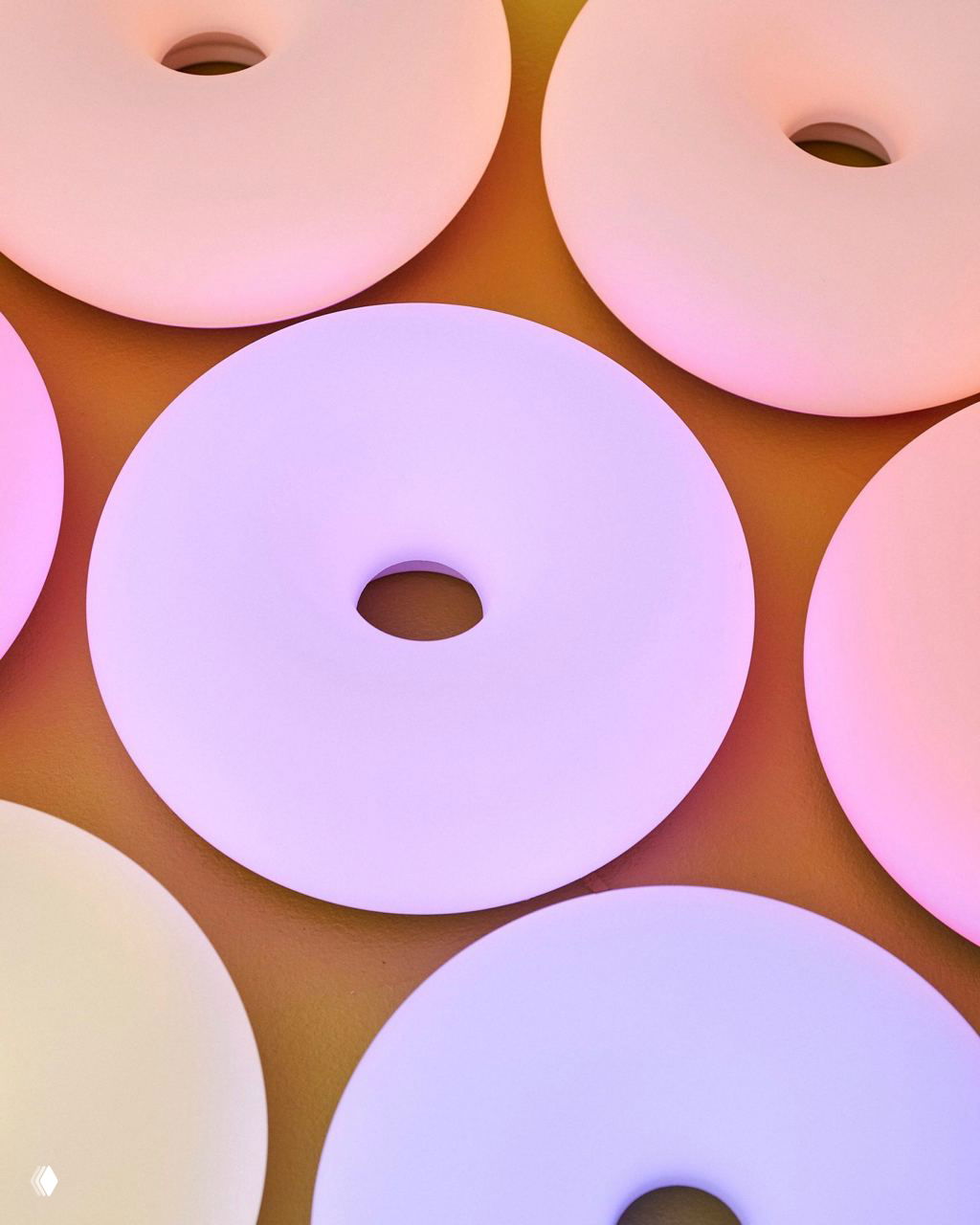 Несколько круглых ламп‑пончиков, выложенных на поверхности, излучают плавные пастельные оттенки от белого до лавандового и нежно‑розового, создавая ритмическую сетку.