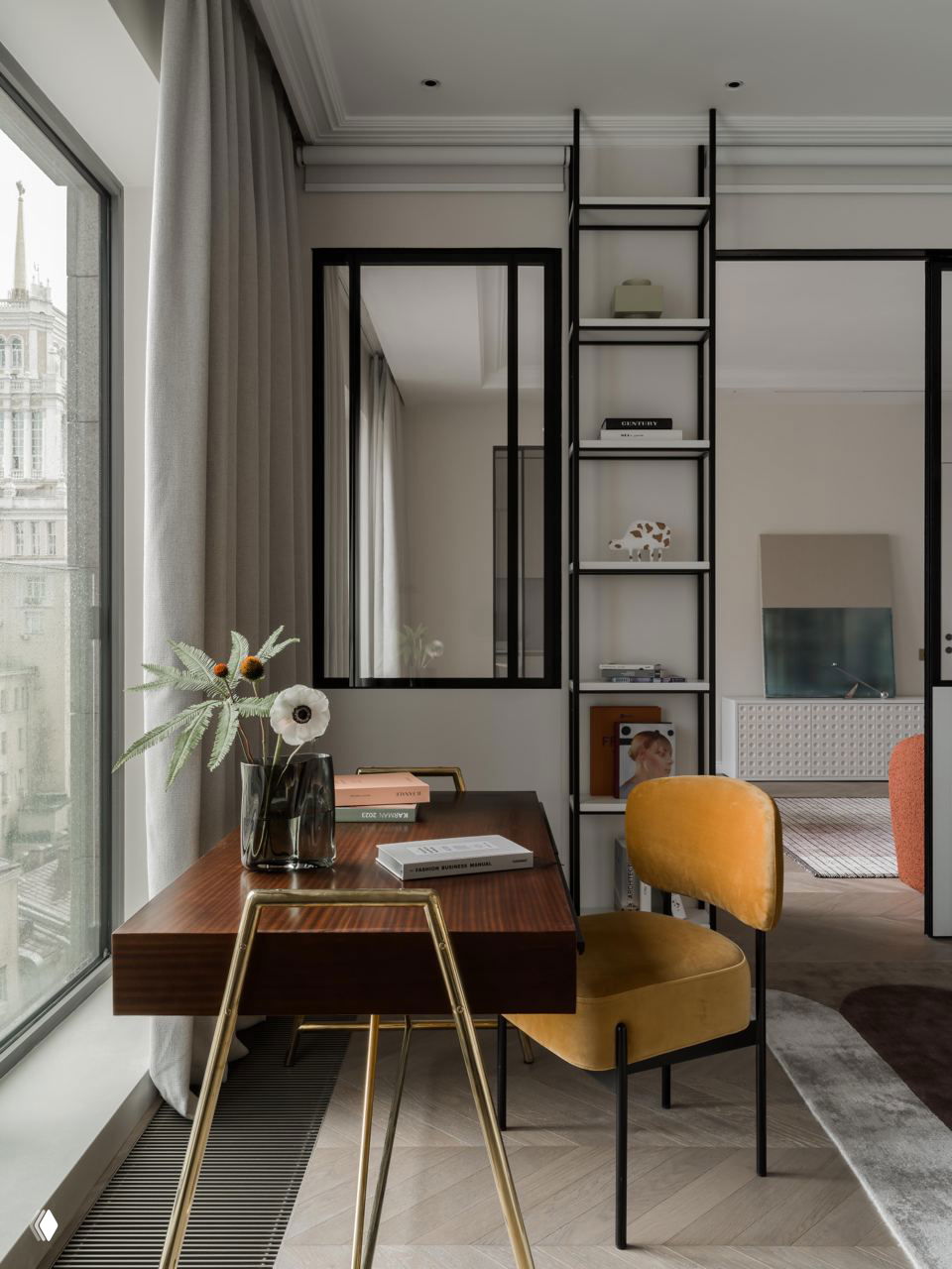 Рабочий уголок у окна: деревянный стол, бархатный жёлтый стул и открытый стеллаж с чёрной металлической рамой, вид на центр Москвы.