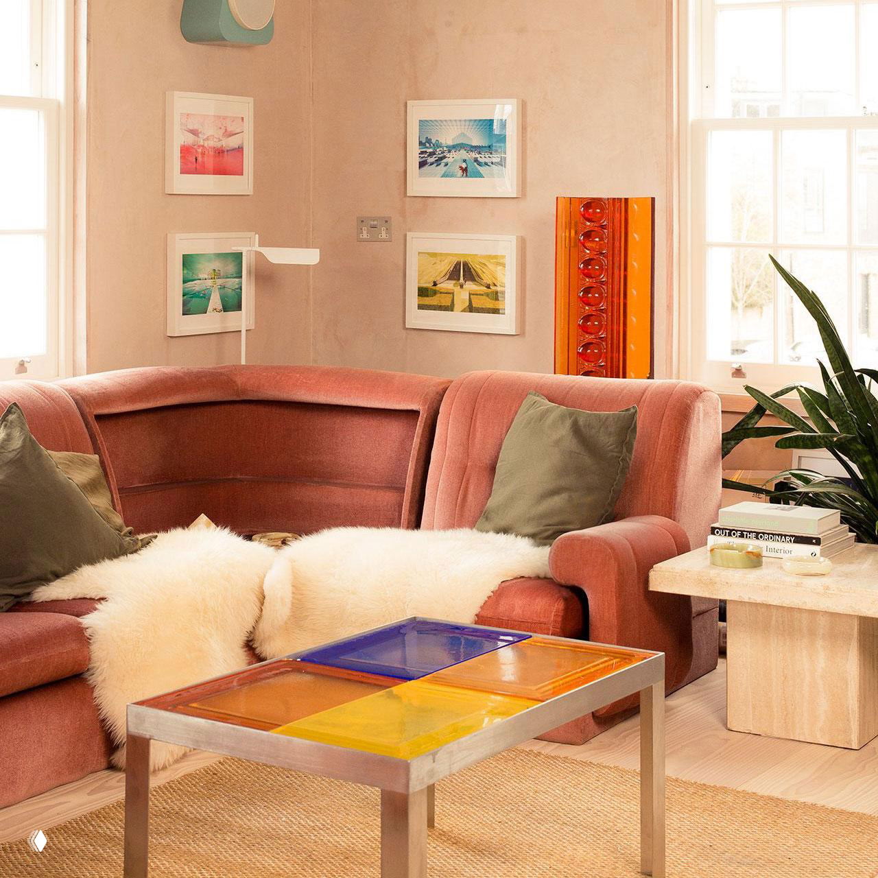 Угловой велюровый розовый диван в тёплой гостиной с декоративными подушками, пушистым пледом и разноцветными настенными арт-работами, уютный ансамбль.