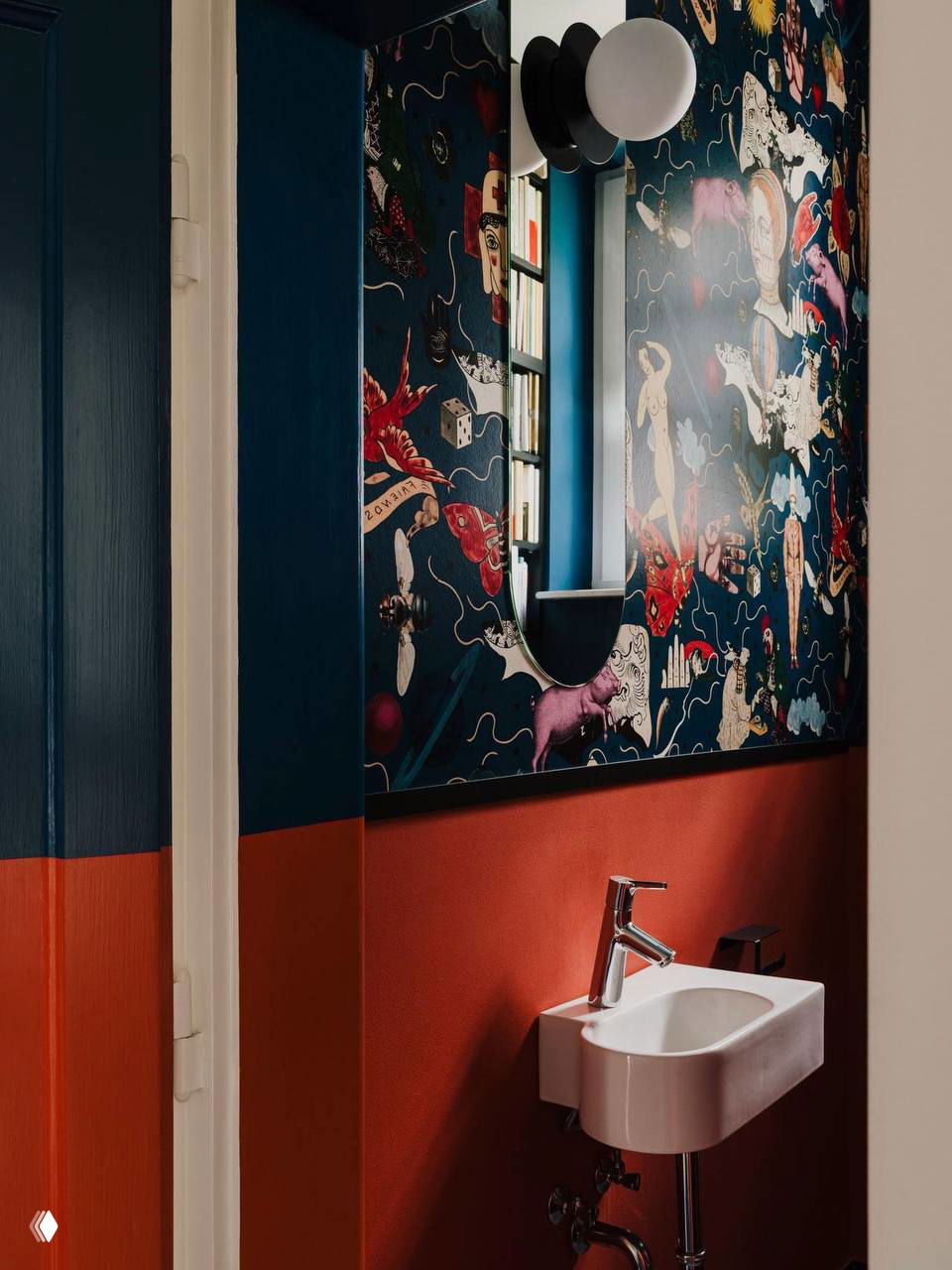 Глубокие тёмно-синие обои с иллюстративными мотивами, полоса терракотового цвета, маленькая белая раковина и зеркало над ней.
