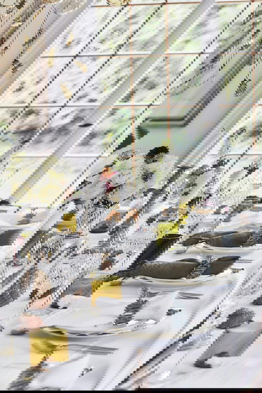 Крупный план сервировки: кристальные бокалы, серебряные подсвечники, салфетки и стеклянные элементы на аккуратной белой скатерти.