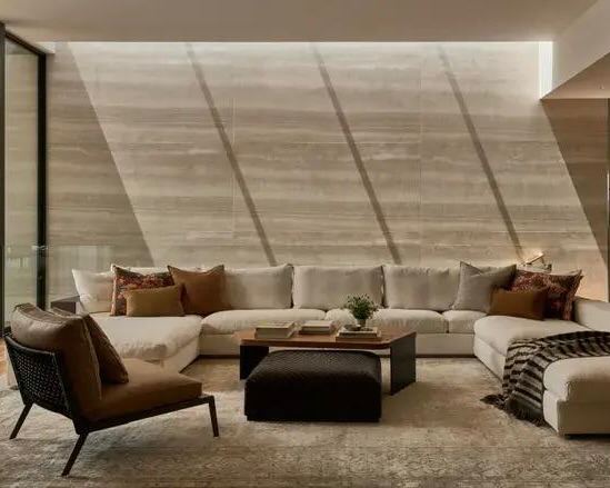 Комфортная гостиная с низким светлым диваном Groundpiece, мягкие подушки, низкие столики и тёплое направленное освещение через окно.