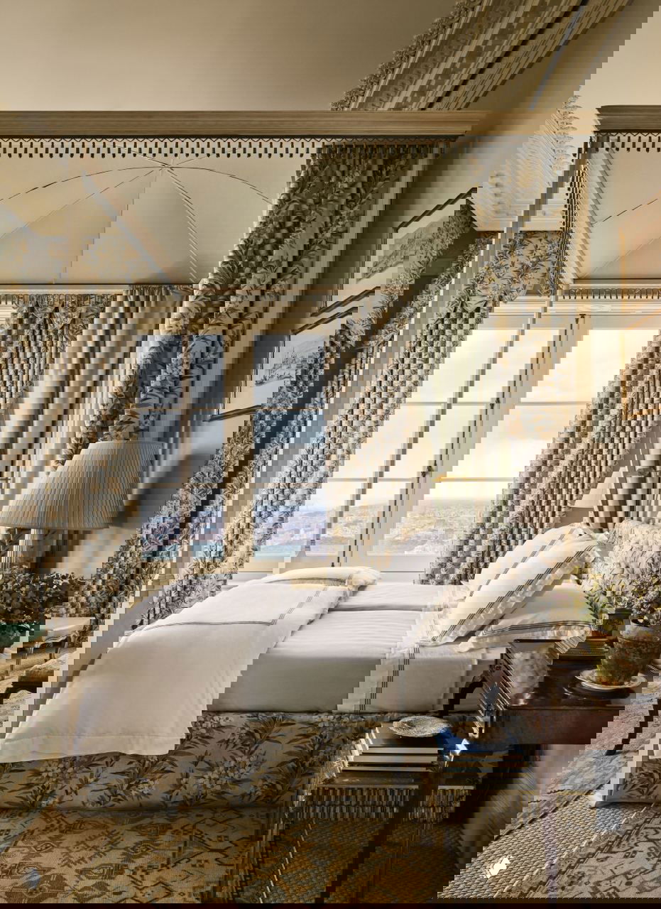 Спальня с балдахином и текстильной отделкой в цветочный рисунок, мягкая цветовая палитра и окна с видом на город — традиционный английский декор в высотке.