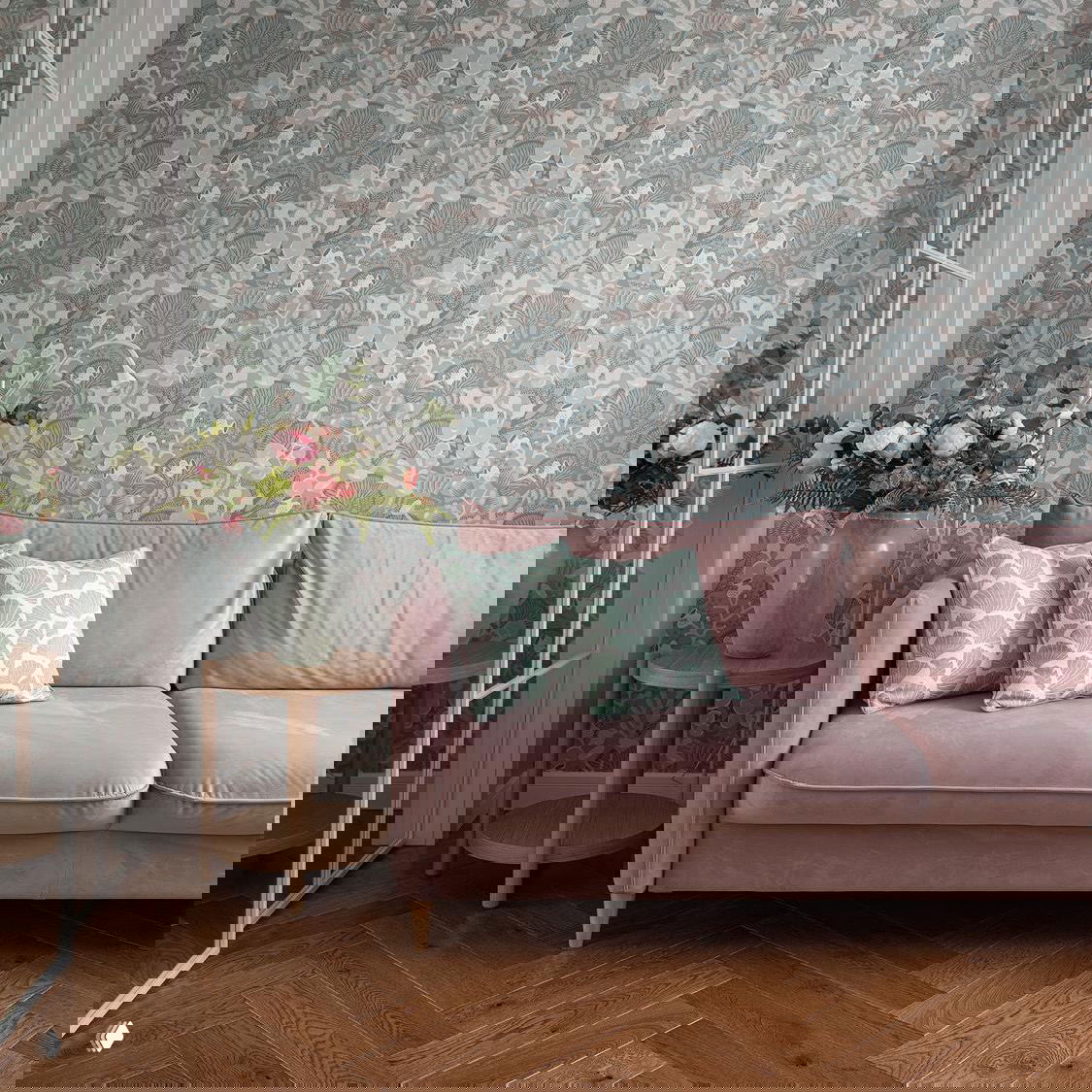 Пыльно-розовый прямой диван на фоне пастельных цветочных обоев; рядом небольшие деревянные столики, вазы с цветами и текстиль в мягких тонах.