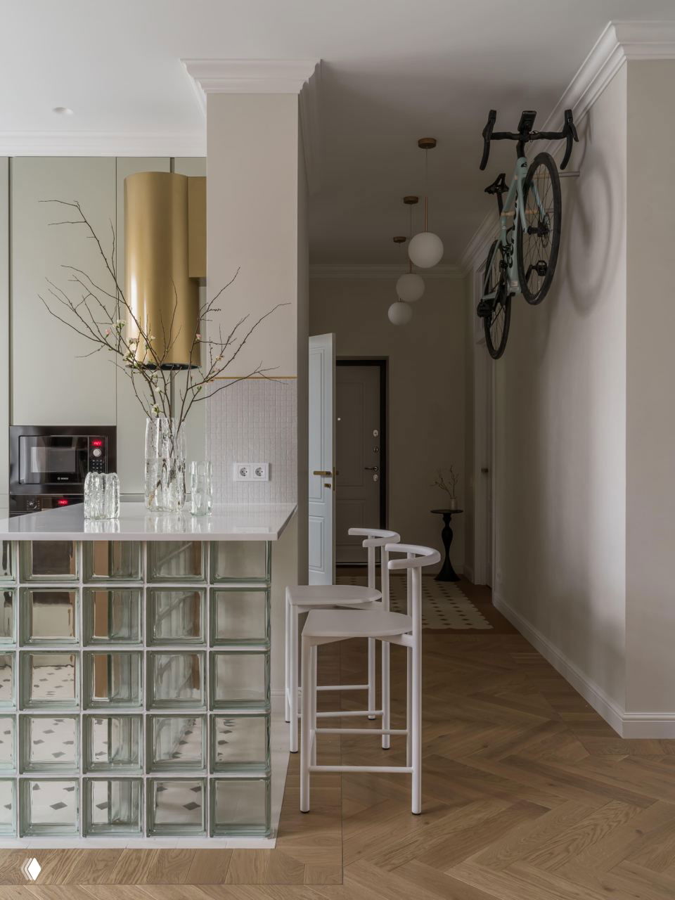 Барная зона и прихожая: стойка из стеклоблоков с белой столешницей, высокие белые стулья, на стене в прихожей закреплён велосипед как элемент хранения.