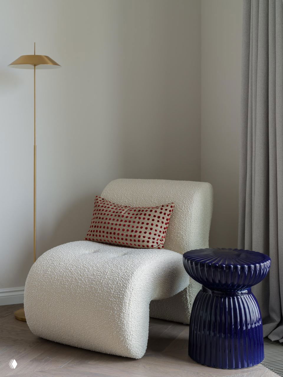 Уютный уголок с креслом в текстуре букле и синей керамической табуреткой на фоне нейтральной стены и мягких штор, минималистичный декор.