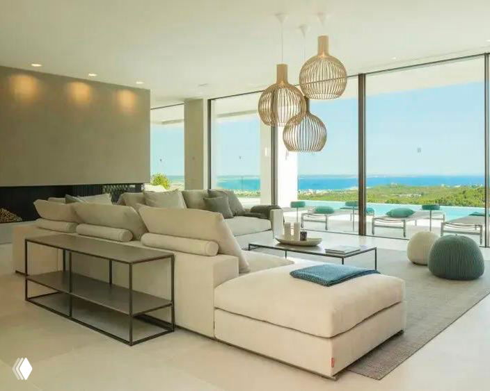 Просторная светлая комната с большими панорамными окнами и пастельным модульным диваном Groundpiece; видна морская панорама за окном.