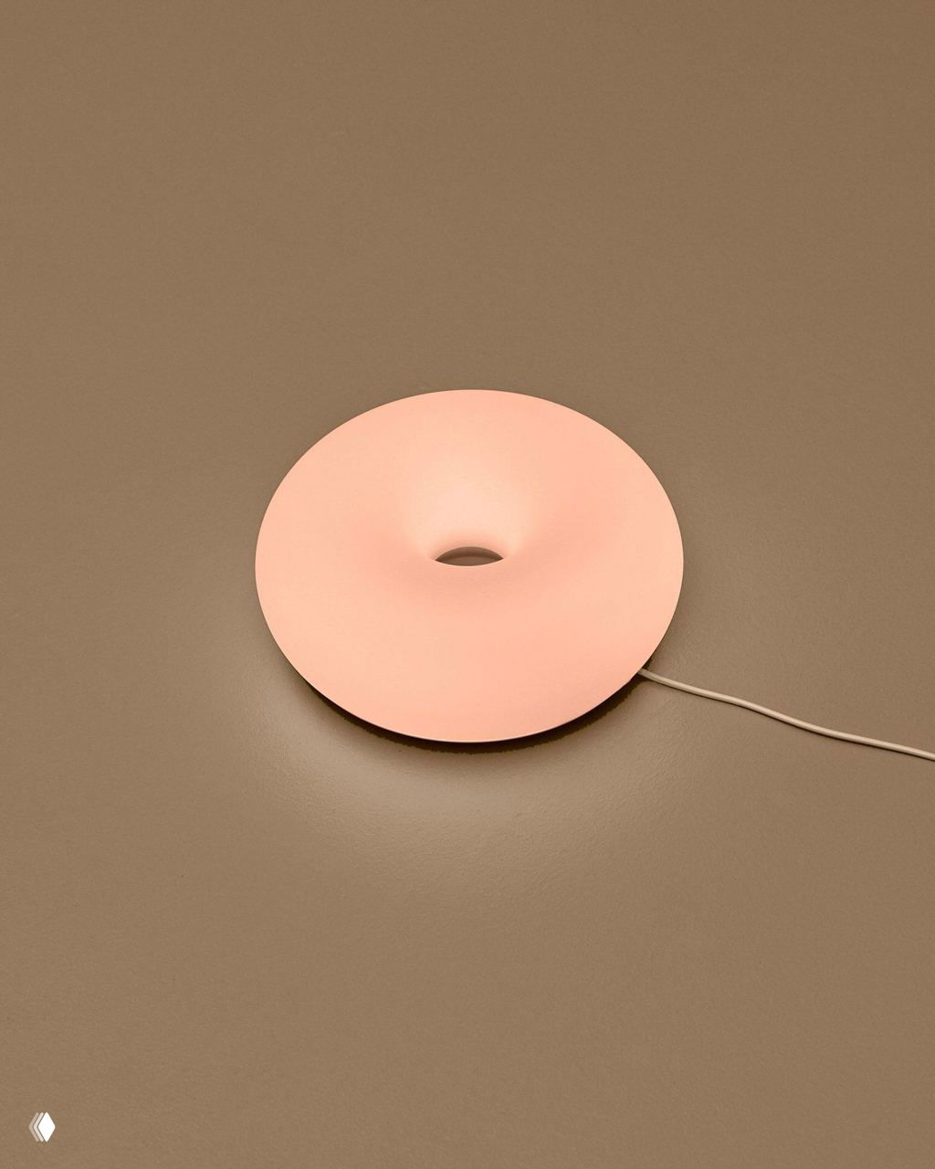 Одиночная круглая лампа‑пончик на нейтральном коричневом фоне с подключённым шнуром, светится бледно‑голубым оттенком в минималистичной презентации продукта.