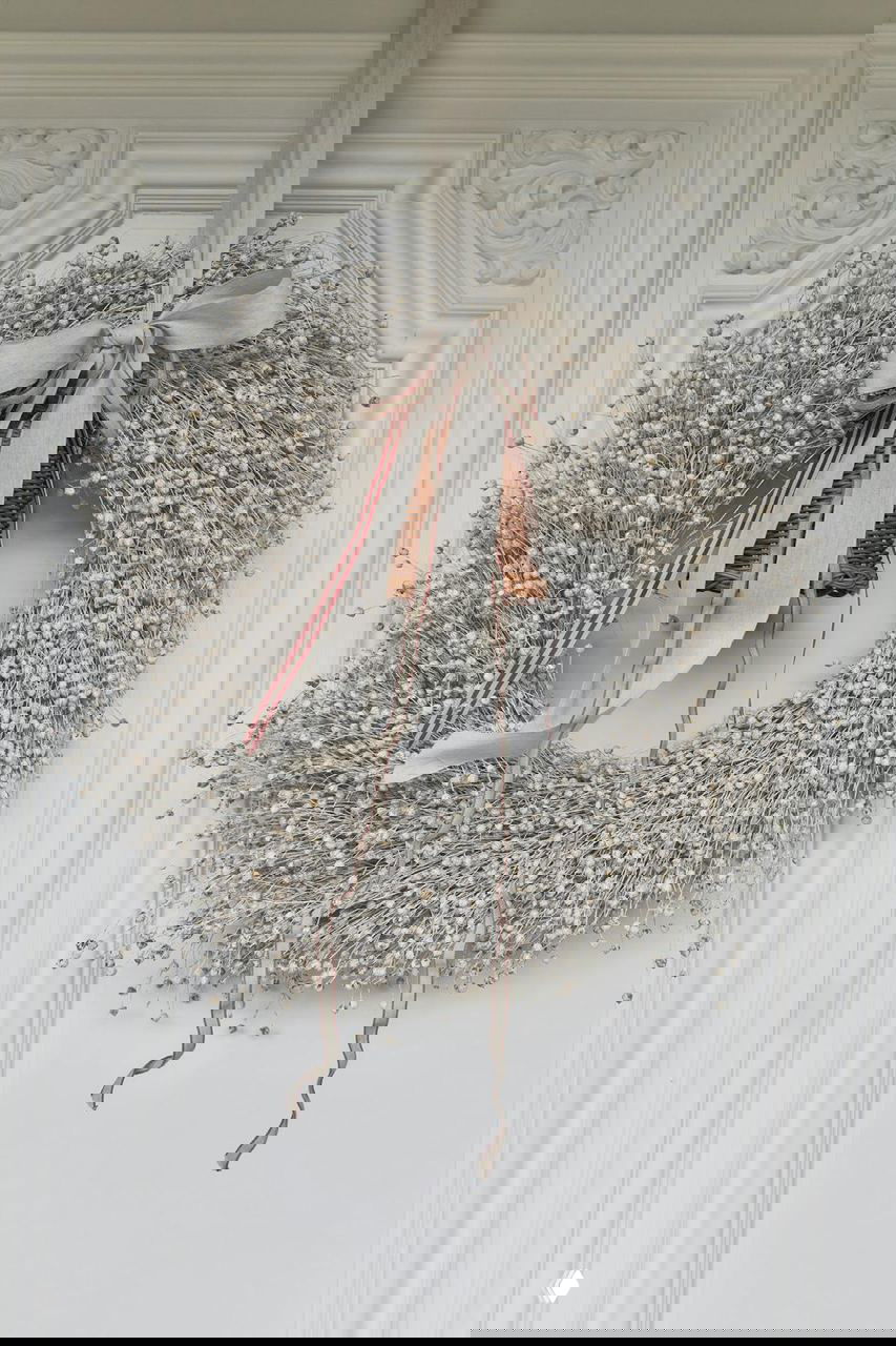 Рождественский венок из сухоцветов и бусин, подвешенный на белой декоративной двери с орнаментом и лепниной, декоративный аксессуар для входа.