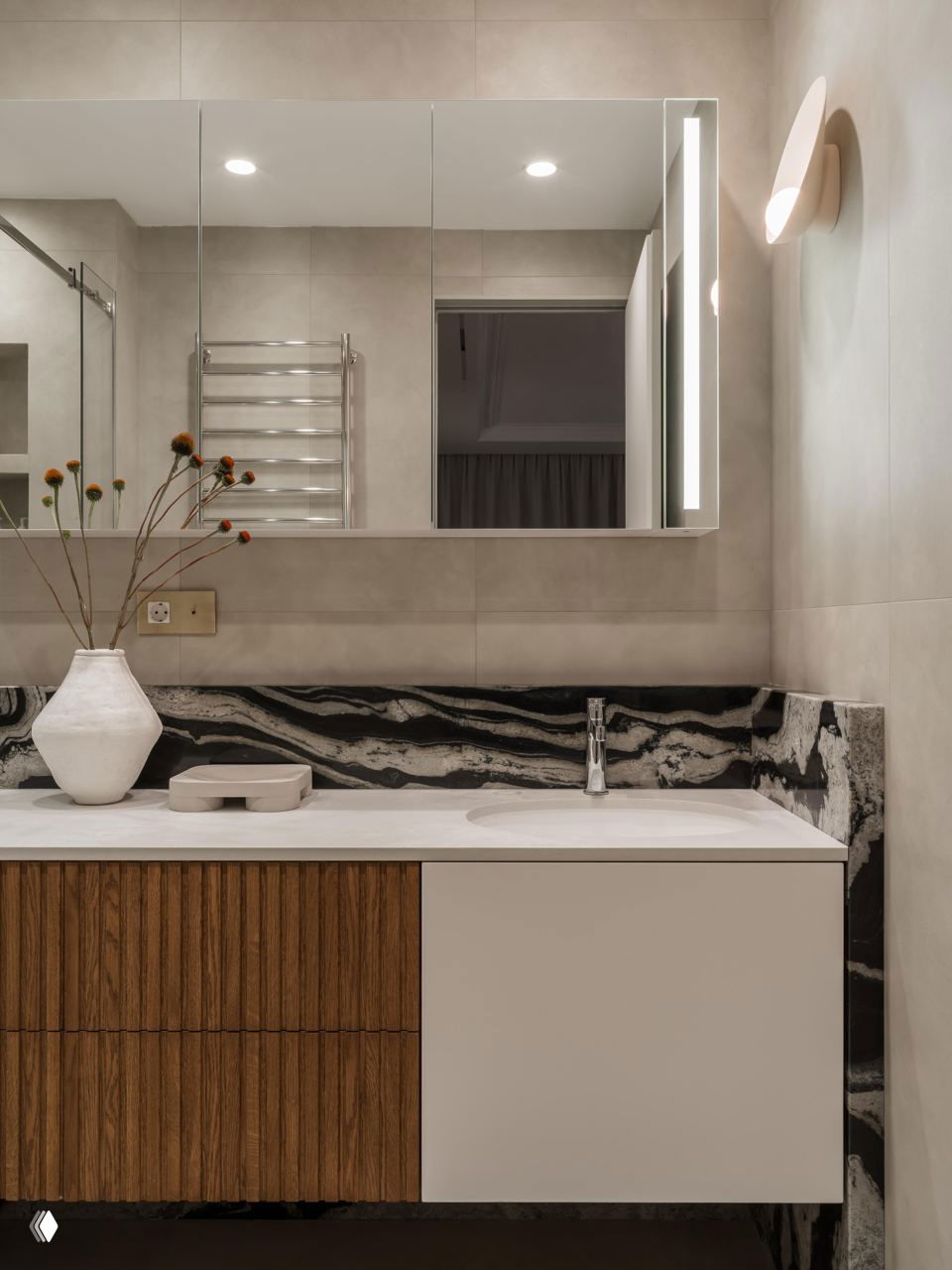Ванная комната апартаментов: мебель с рифлеными деревянными фасадами, белая раковина и чёрно-белая мраморная столешница, сдержанный интерьер.