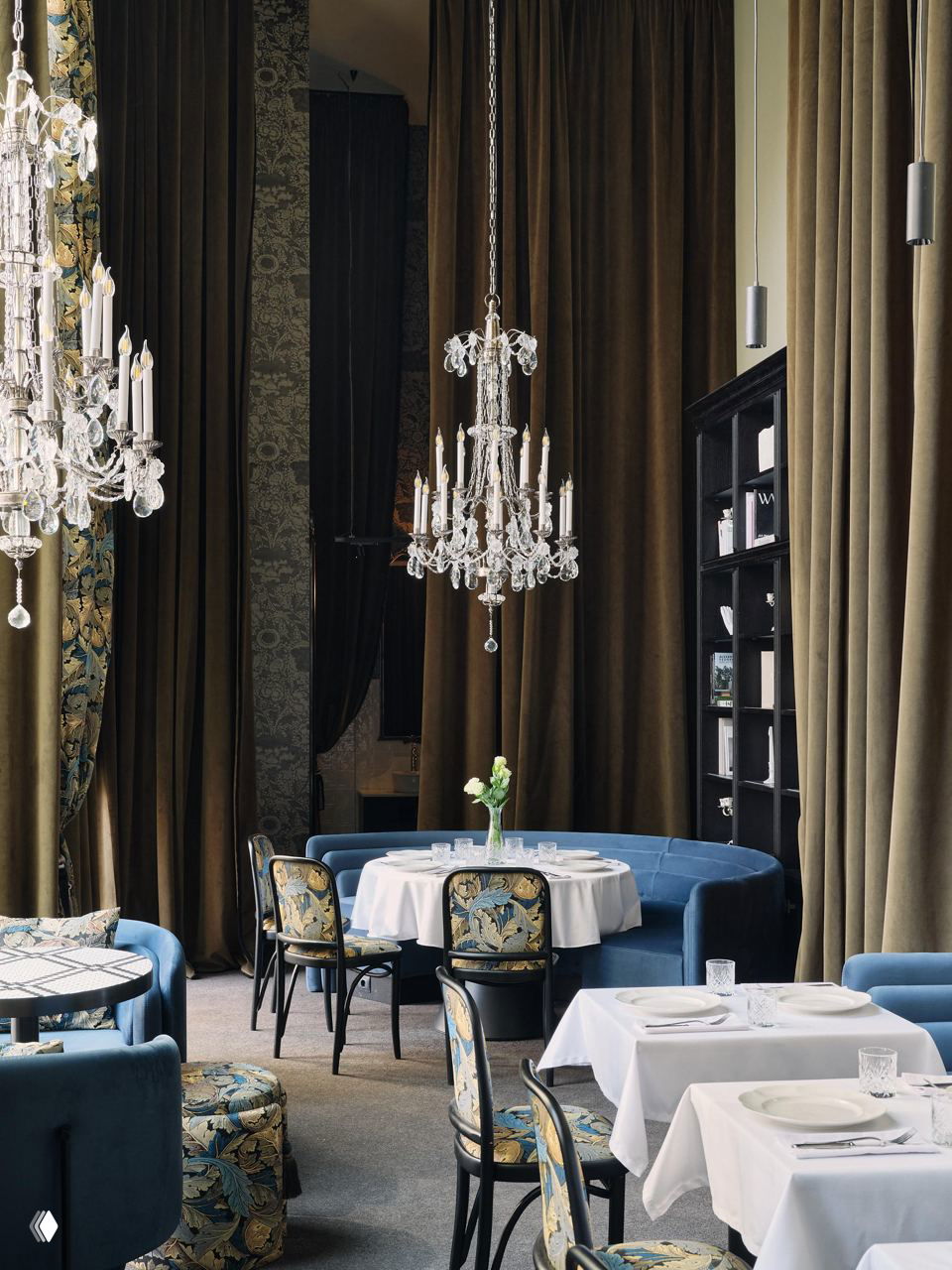 Банкетная зона с круглыми диванами и хрустальными люстрами, столики с белыми скатертями и стулья с узорной обивкой на фоне высоких штор.