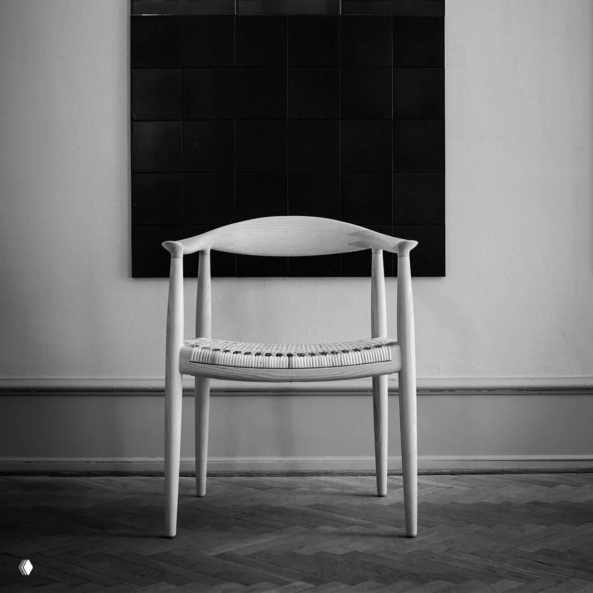 Фотография светлого деревянного кресла с плетёным сиденьем и изящной изогнутой спинкой на фоне строгой геометрии стены.