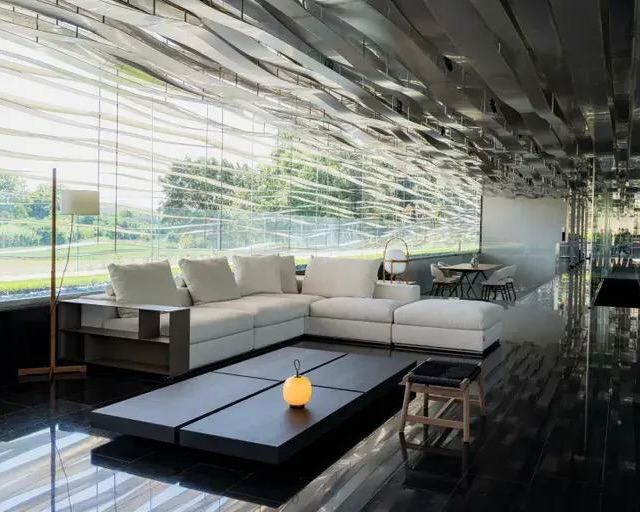 Современный интерьер с чёрным глянцевым полом и белым модульным диваном Groundpiece на переднем плане, низкий стол и минималистская мебель.