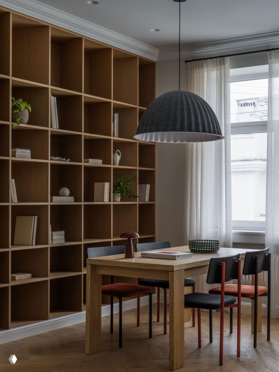 Столовая зона с большой деревянной полкой-стеллажом в ячейках, деревянный стол и разноцветные стулья, объёмный подвесной светильник над столом.