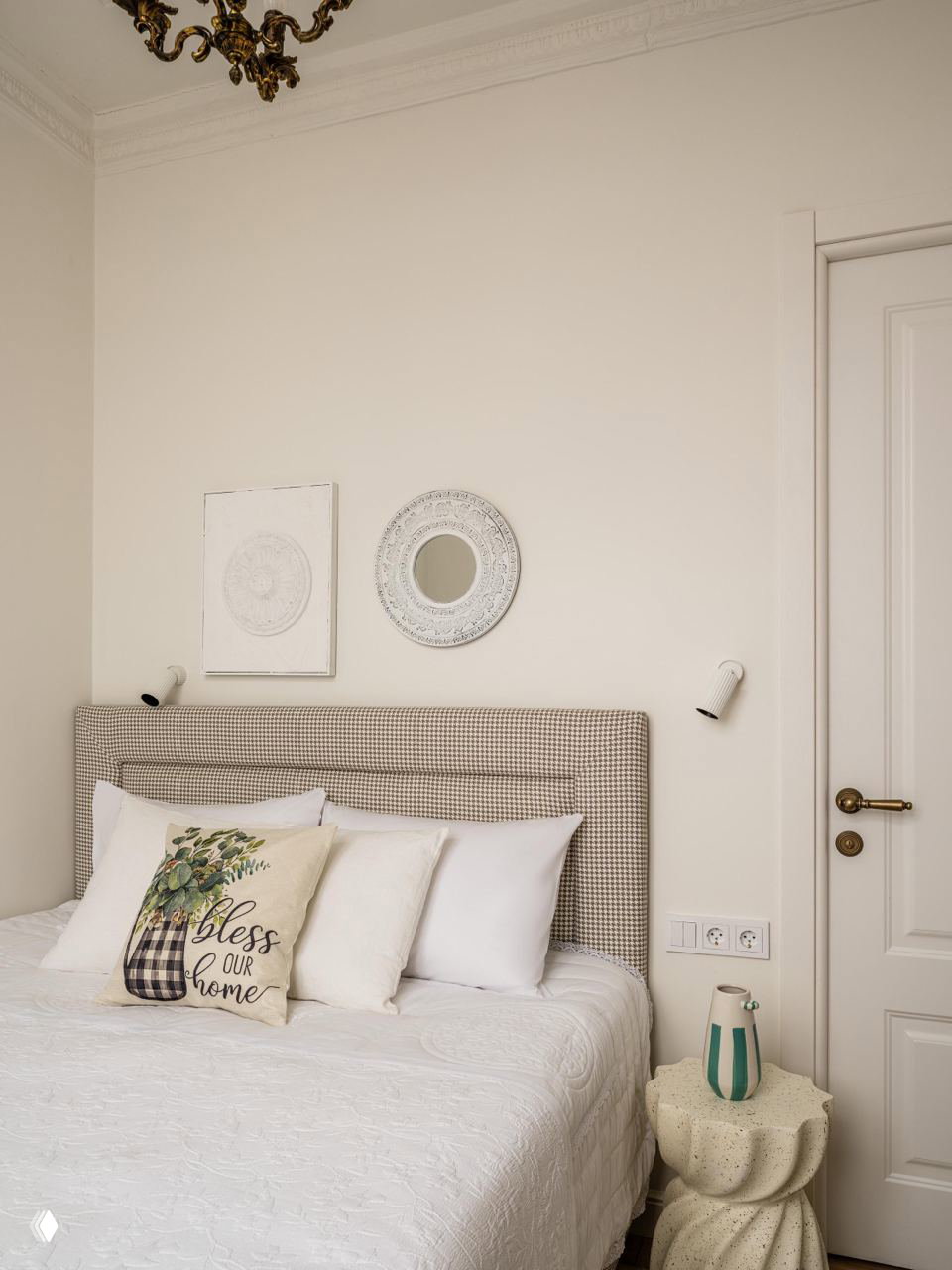 Спальня в пастельных тонах: высокая стёганая спинка кровати в мелкую клетку, белое покрывало и декоративные подушки на светлом фоне.