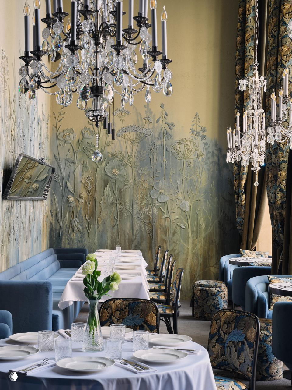 Сервированные столы у стены с декоративным рельефным растительным орнаментом, мягкие синие диваны и стеклянные бокалы в интерьере ресторана.