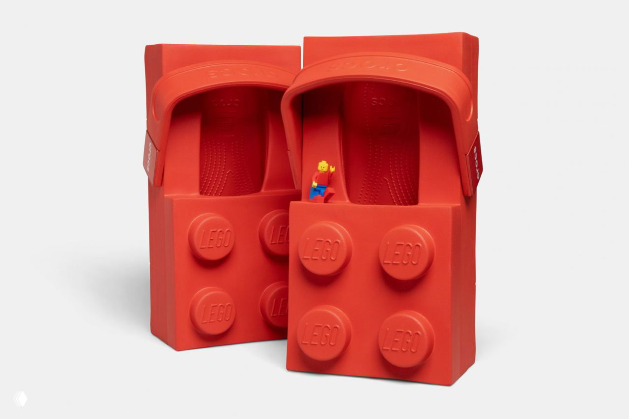 Пара ярко-красных сабо LEGO Brick Clog, крупный план, вид сверху и спереди; в одной обуви видно миниатюрную фигурку LEGO.