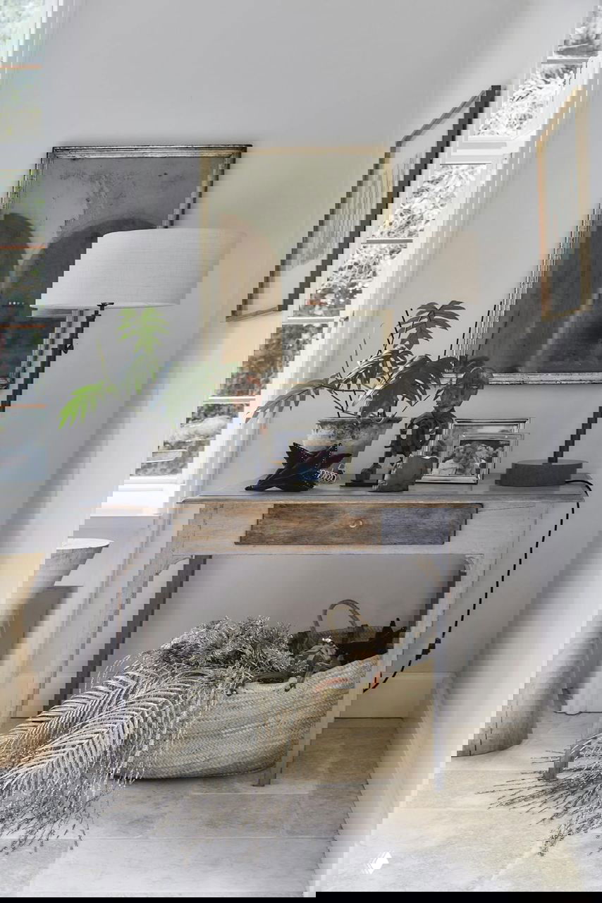 Угловой столик с лампой, семейными фотографиями и корзиной с декором на светлом фоне интерьера, акцент на уюте и деталях.